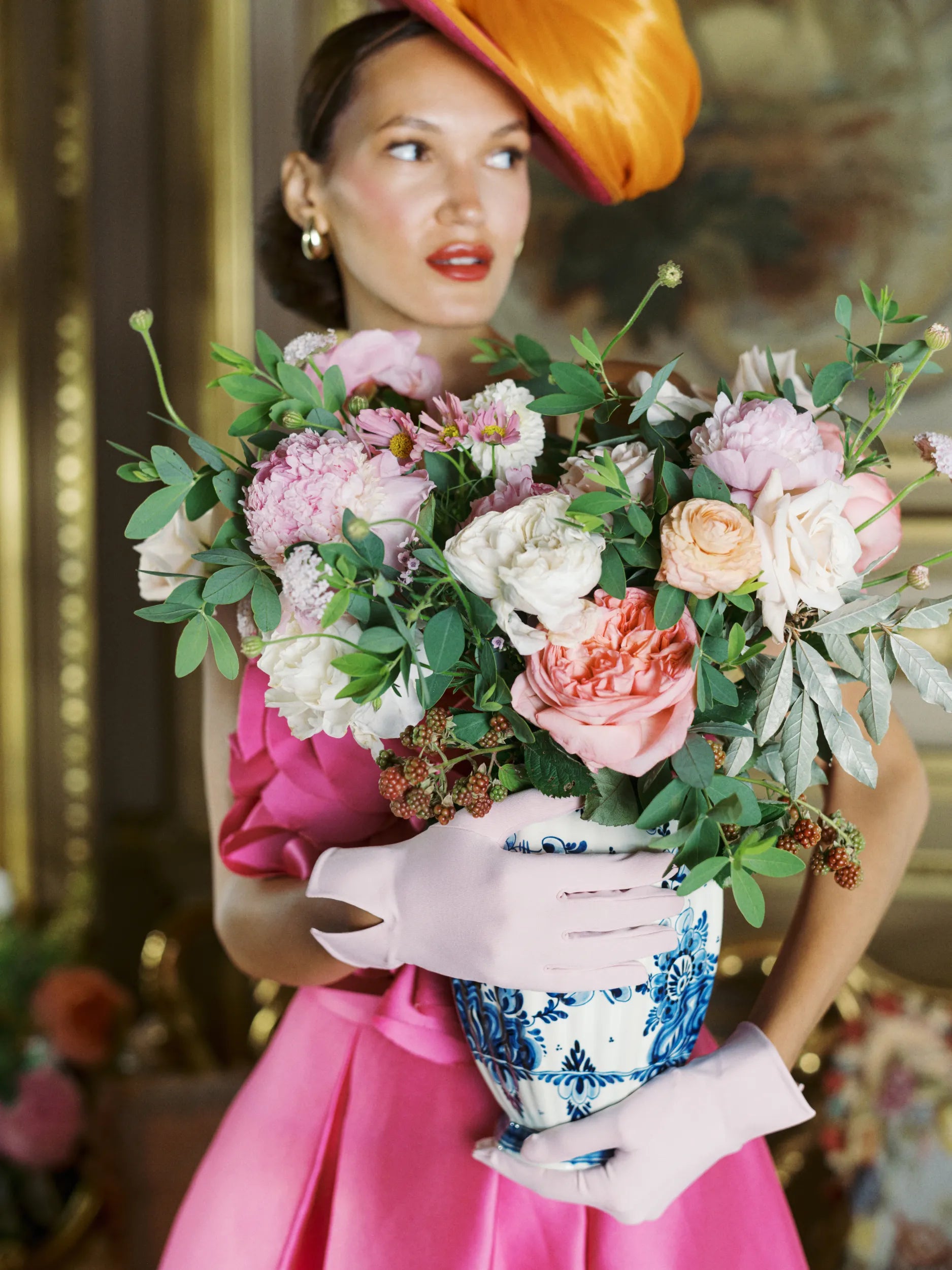 Woman looking away, wearing light pink day gloves holding flower vase.