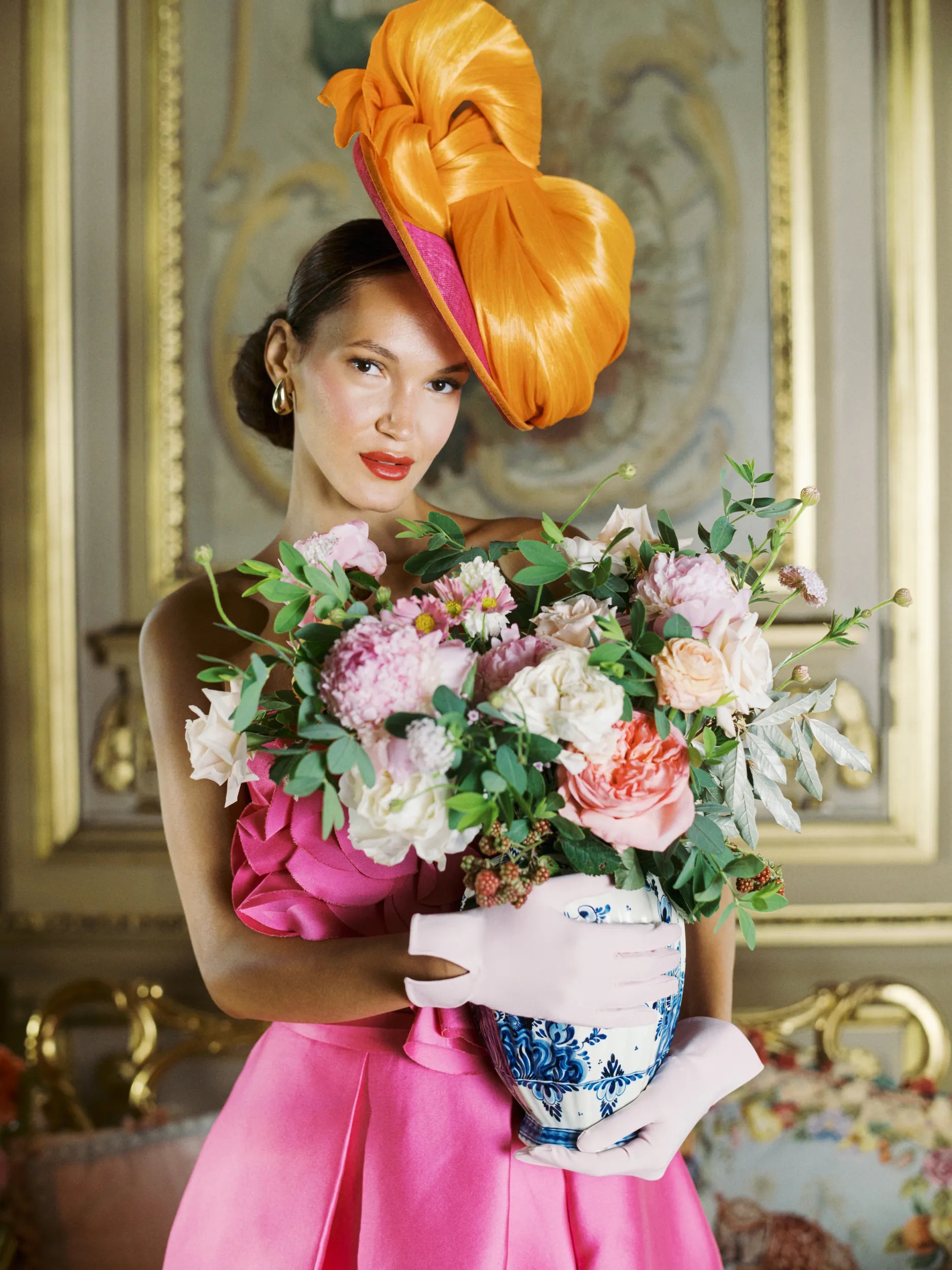 Woman holding a vase of flowers wearing light pink day gloves.