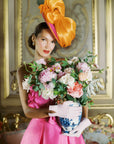 Woman holding a vase of flowers wearing light pink day gloves.