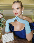 Glamorous woman wearing light blue gloves with hands on chin.