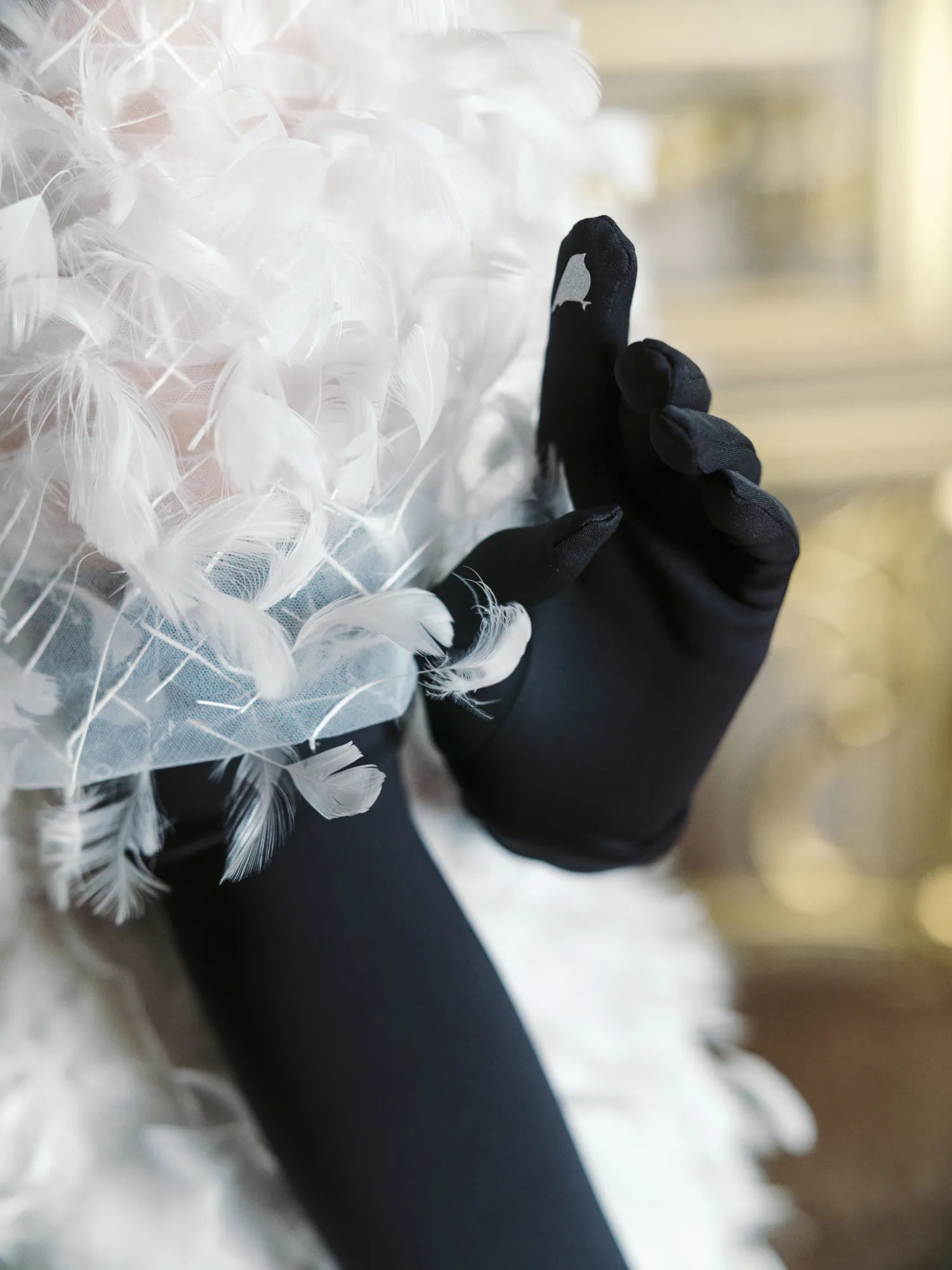 Woman wearing white feather dress wearing opera, long black gloves showing the technology touchscreen finger.