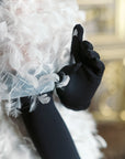 Woman wearing white feather dress wearing opera, long black gloves showing the technology touchscreen finger.