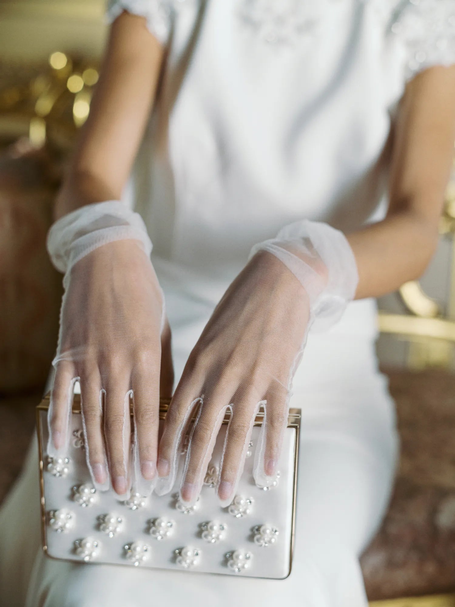 Woman in wedding dress wearing tulle white gloves holding white satin clutch.