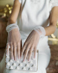Woman in wedding dress wearing tulle white gloves holding white satin clutch.
