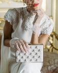 Woman in wedding dress wearing tulle white gloves holding white satin clutch.