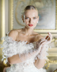 Woman in white feather dress, wearing white mid length tulle gloves.