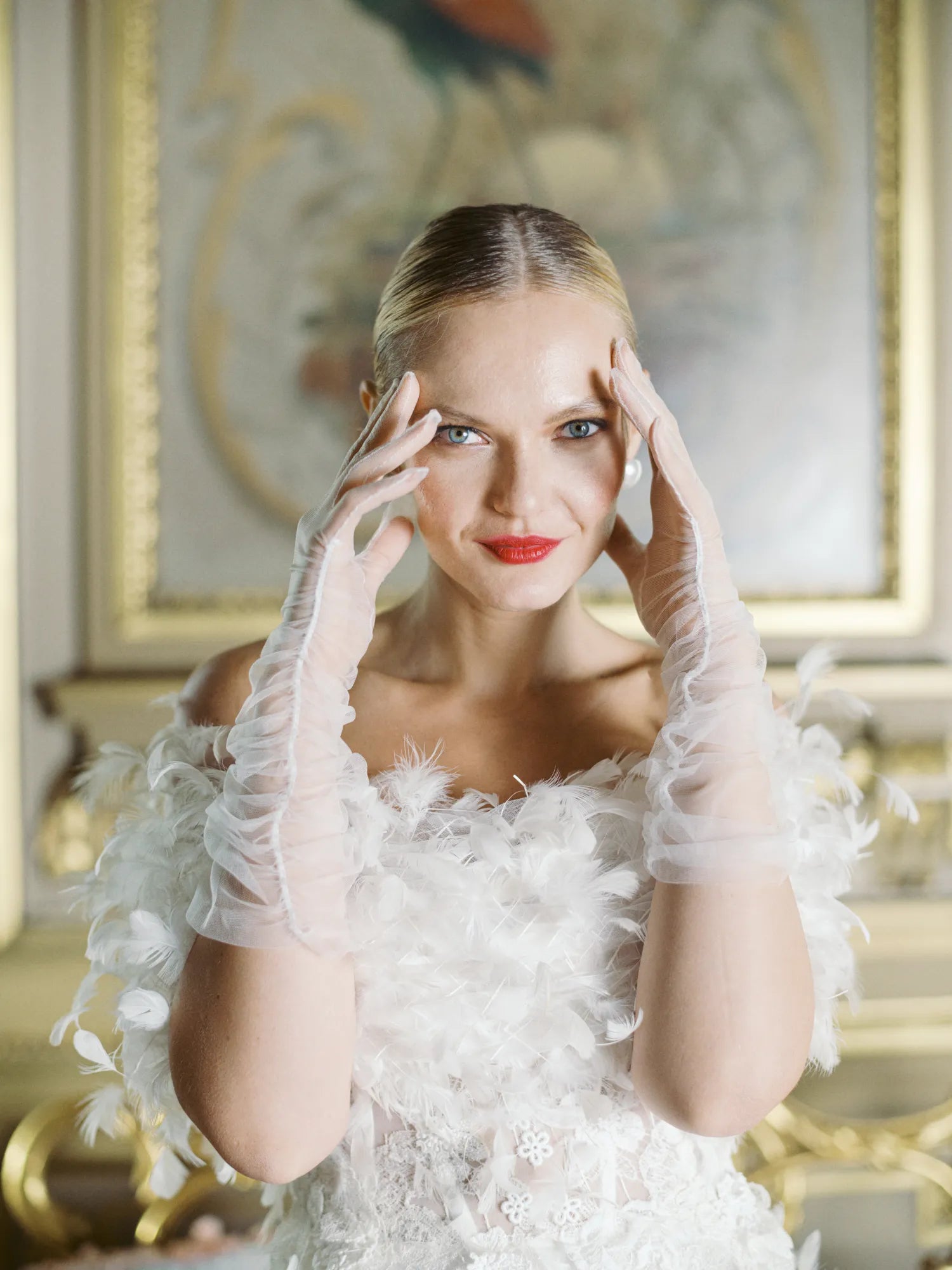 Woman, smiling with hands up to head wearing white tulle, mid length gloves.