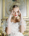 Woman, smiling with hands up to head wearing white tulle, mid length gloves.