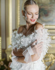 Bride holding arms, wearing white, ruched, tulle wrist length gloves.