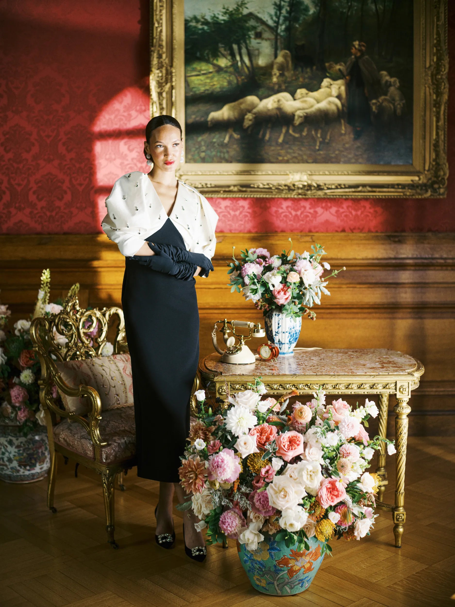 Woman stands poised with folded hands wearing elbow black long gloves.