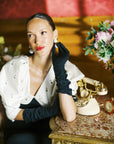A woman in a black dress and THE STEPHANIE - Long Gloves Black by LadyFinch sitting on a table.