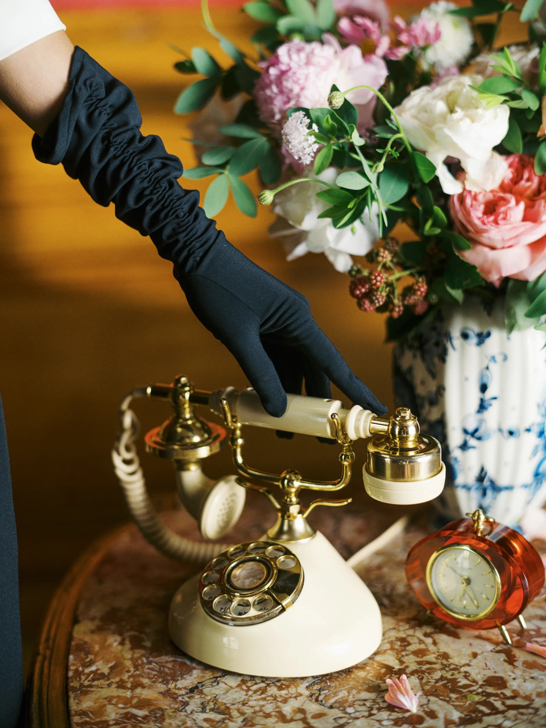 Woman's hand touches vintage phone wearing long black elbow gloves.