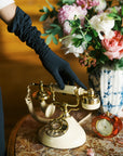 Woman's hand touches vintage phone wearing long black elbow gloves.