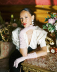 An elegant woman sitting at vintage table wearing pink elbow gloves.
