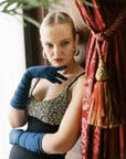 A woman standing, poised, wearing elbow length, dark blue gloves.