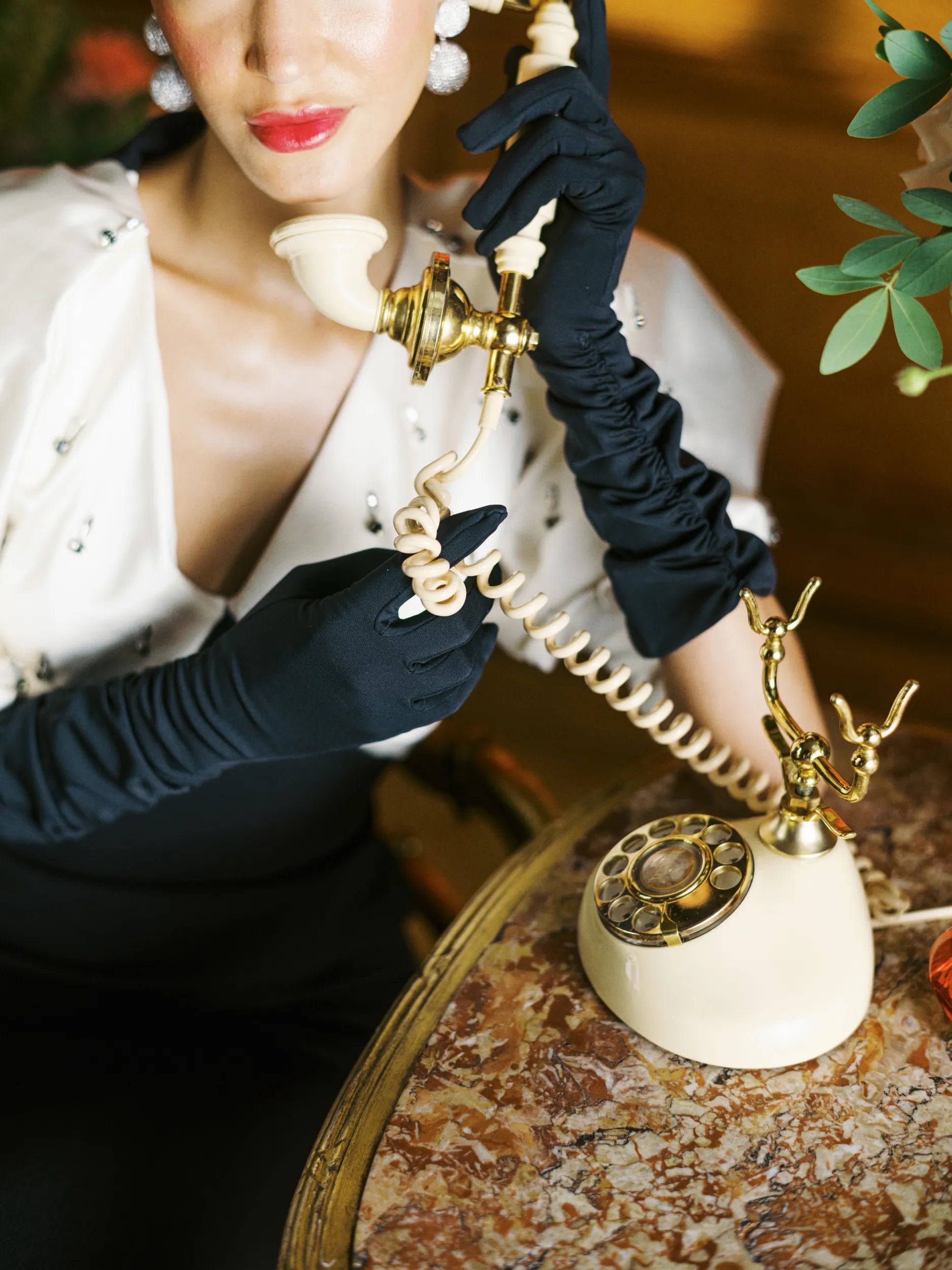 Woman wearing long black gloves holding vintage phone.