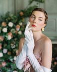 A woman in THE SUNNY - White Opera Gloves by LadyFinch exuding high-fashion elegance while posing for a photo at formal events.