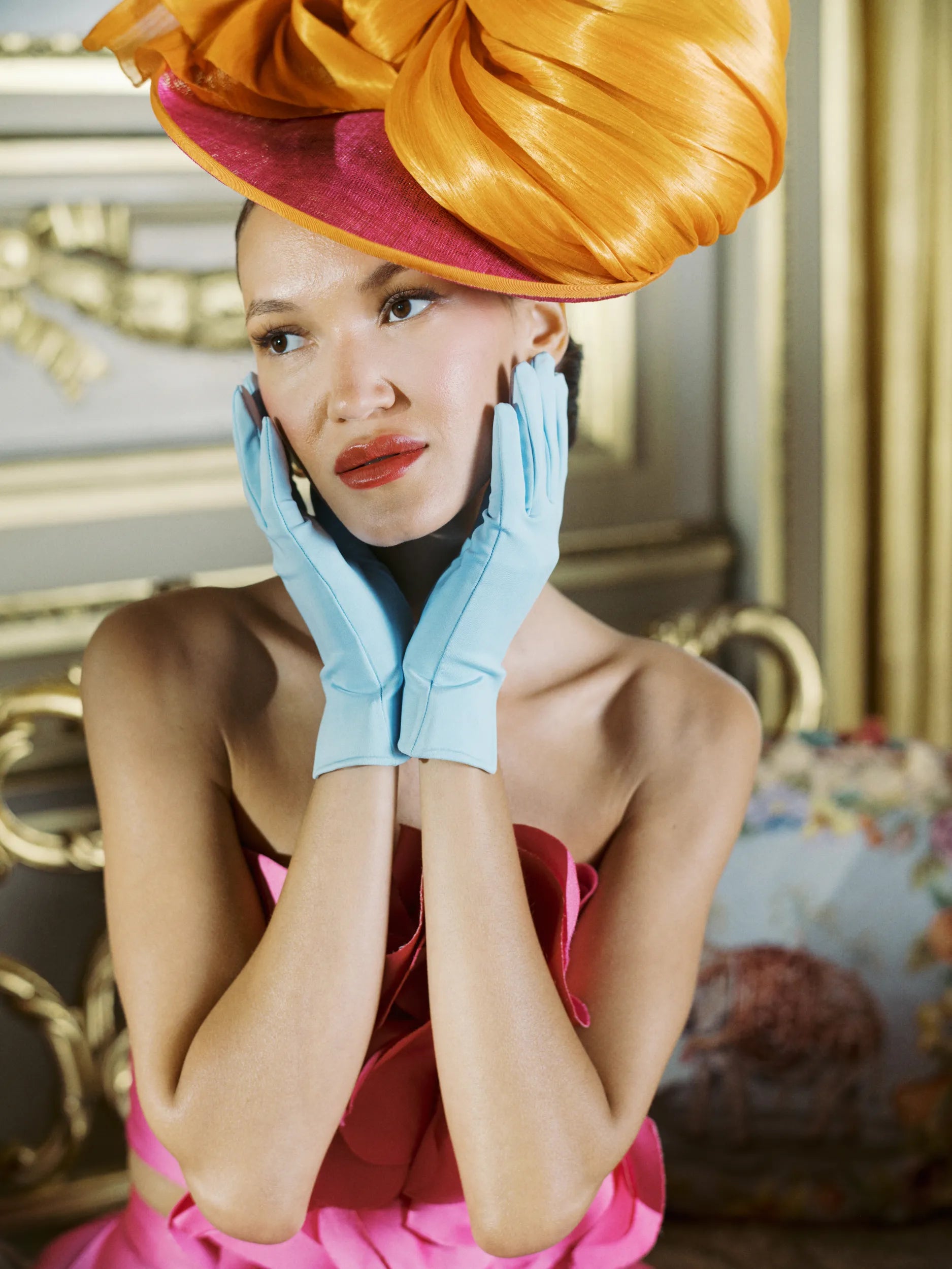 Woman at high tea wearing light blue gloves with hands elegantly on her face.