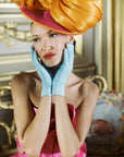 Woman at high tea wearing light blue gloves with hands elegantly on her face.