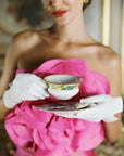 Woman holding tea cup with elegant white day gloves.