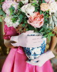 Woman wearing light pink wrist gloves holding large vase of flowers.