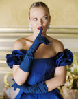 Women wearing blue dress and blue gloves holding finger to mouth.