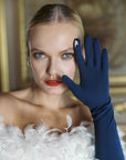 Glamorous woman wearing over the elbow blue opera gloves with palm open to show technology touchscreen index finger.