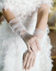 Woman in white dress, holding out hands wearing white fitted tulle gloves.