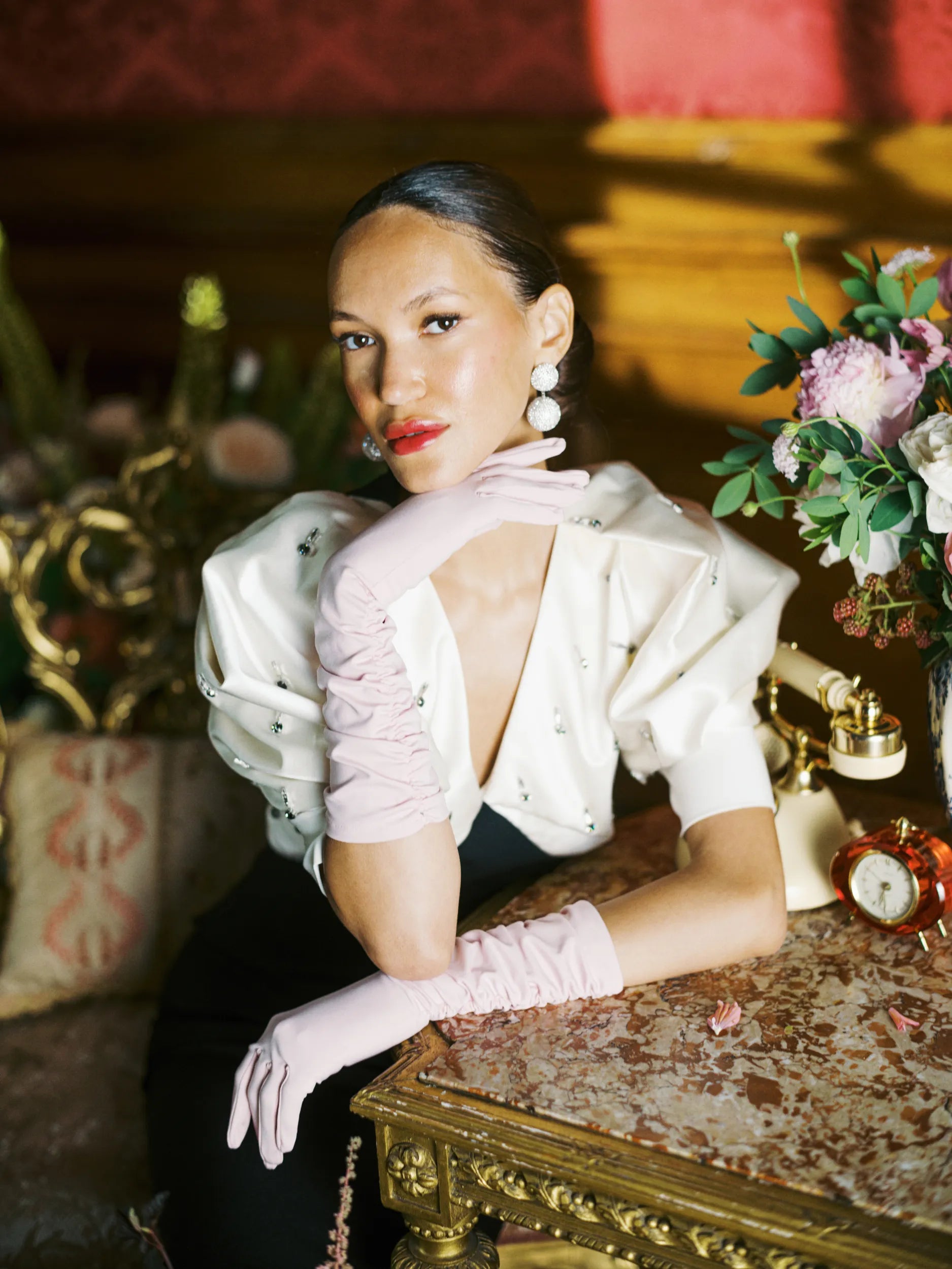 An elegant woman sitting at vintage table wearing pink elbow gloves.