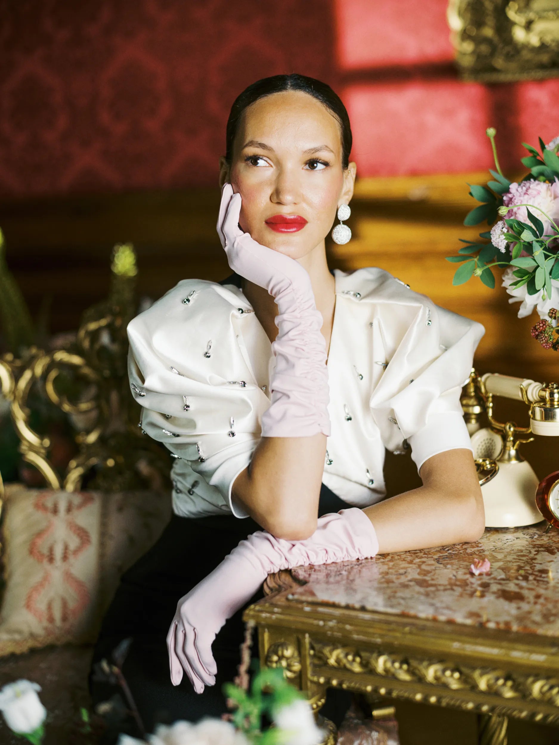 Woman sits, poised, wearing pink, elbow length gloves.