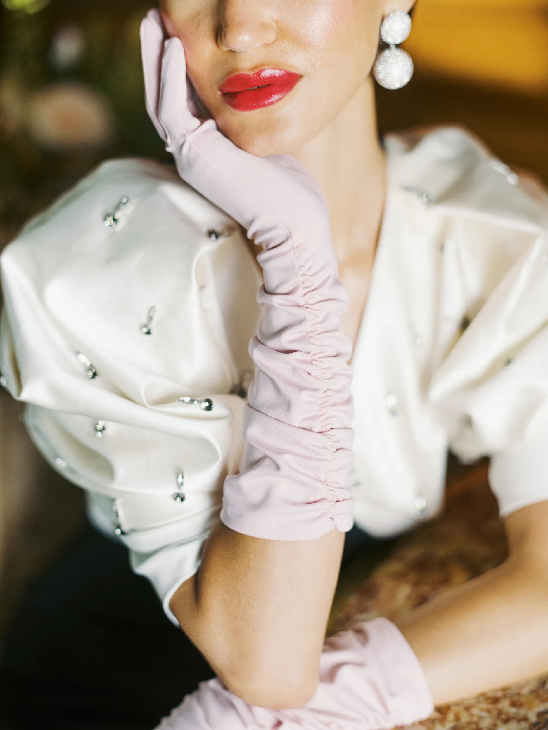 A glamorous woman rests her head in her hand, wearing pink elbow, long gloves.