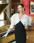 Elegant woman stands new piano, wearing elbow length long light blue gloves.