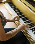 Woman wearing elbow length, long, beige, formal gloves, playing the piano.