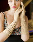 Glamorous, woman holding hands up, wearing elbow length, long formfitting, beige gloves.