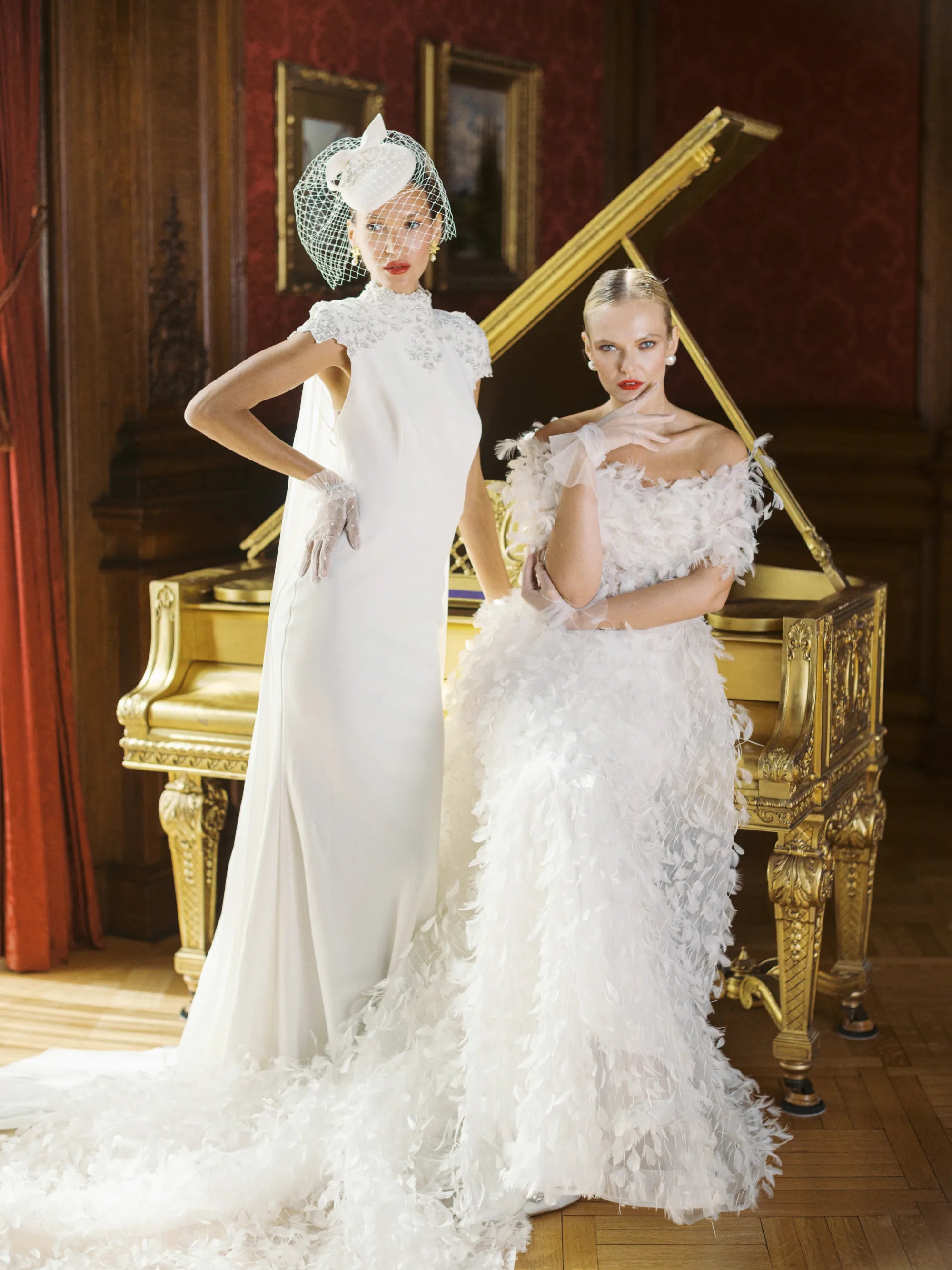 Two brides in white dress and white bridal gloves sitting near gold piano.